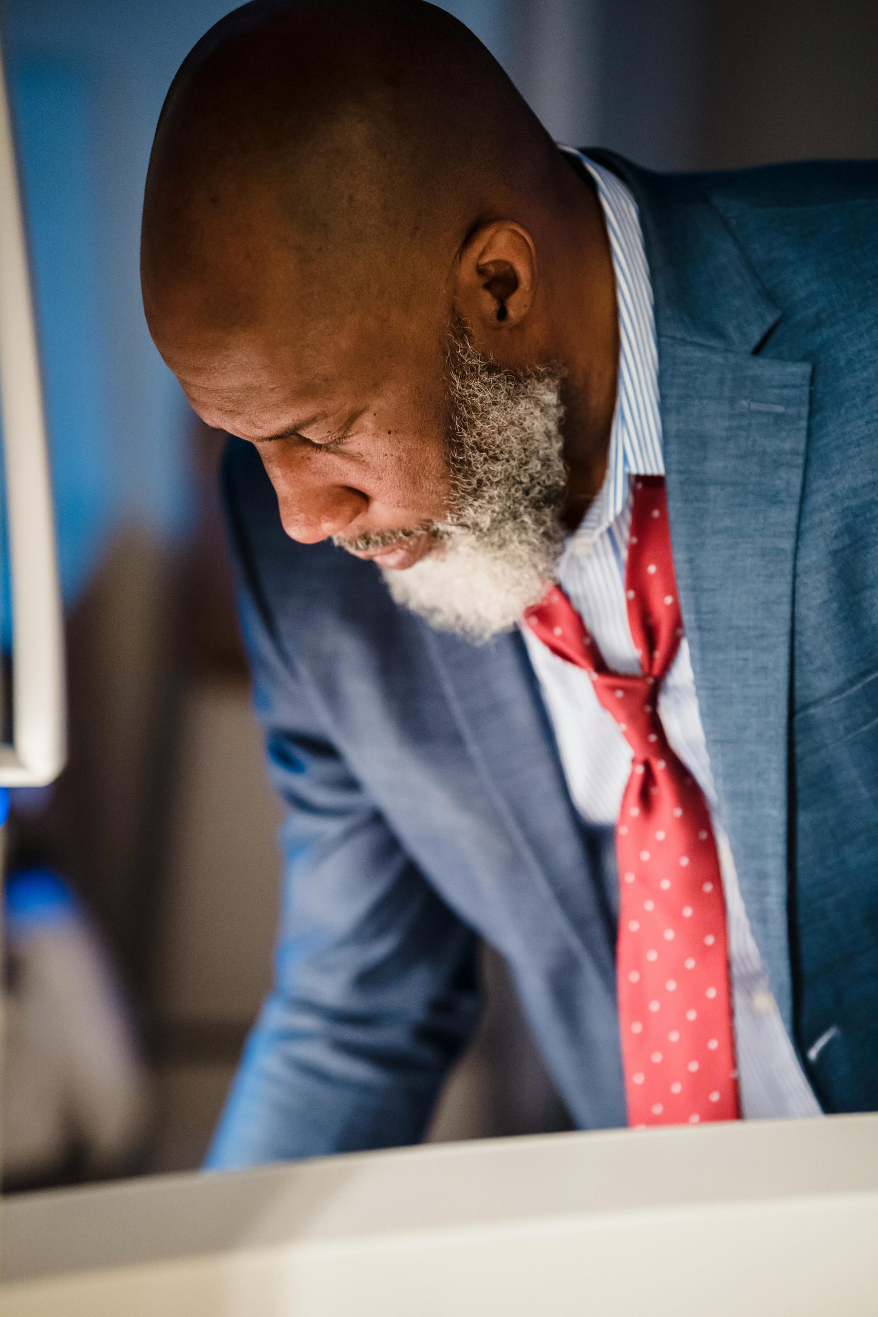 Close-up of a distinguished bearded man in a suit leaning over, focused and thoughtful.